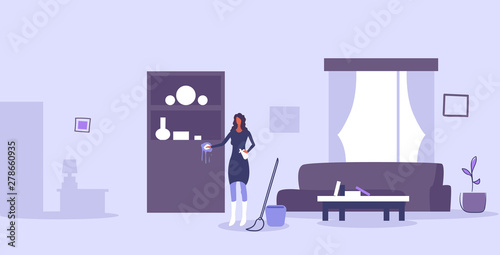 housewife cleaning furniture girl wiping dust with duster and spray household concept woman doing housework modern living room interior horizontal full length