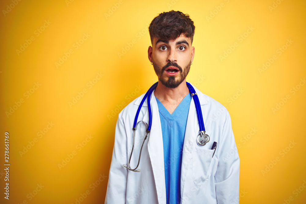 Young doctor man with tattoo wearing stethocope standing over isolated yellow background afraid and shocked with surprise expression, fear and excited face. Young doctor man with tattoo wearing stethocope standing over isolated yellow background afraid and shocked with surprise expression, fear and excited face.