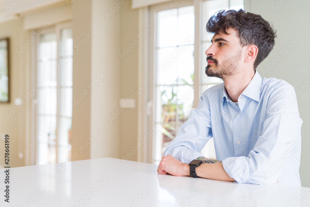 Young businesss man sitting on white table looking to side, relax profile pose with natural face with confident smile.