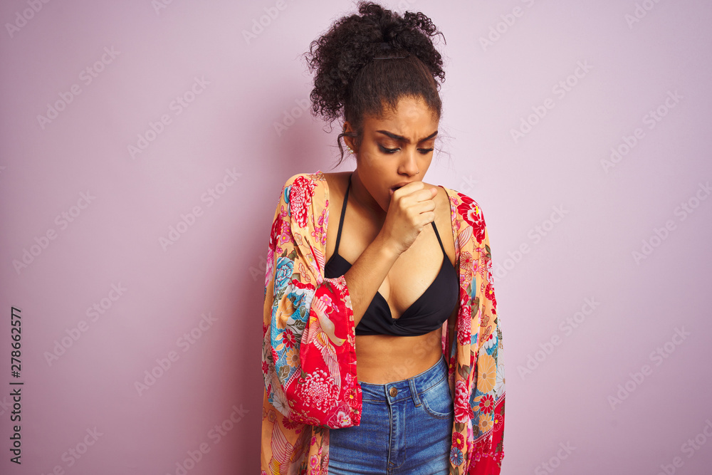 American woman on holiday wearing bikini and colorful dress over isolated pink background feeling unwell and coughing as symptom for cold or bronchitis. Healthcare concept. American woman on holiday wearing bikini and colorful dress over isolated pink background feeling unwell and coughing as symptom for cold or bronchitis. Healthcare concept.