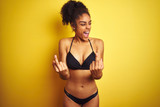 African american woman on vacation wearing bikini standing over isolated yellow background Showing middle finger doing fuck you bad expression, provocation and rude attitude. Screaming excited