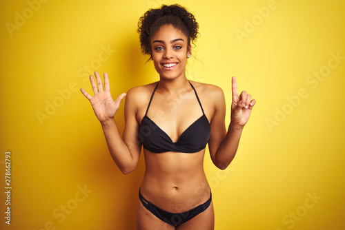 African american woman on vacation wearing bikini standing over isolated yellow background showing and pointing up with fingers number six while smiling confident and happy.