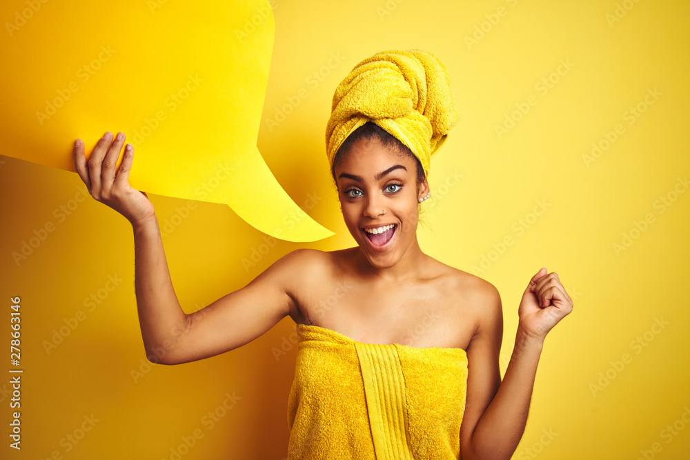 Afro woman wearing towel after shower holding speech bubble over isolated yellow background screaming proud and celebrating victory and success very excited, cheering emotion