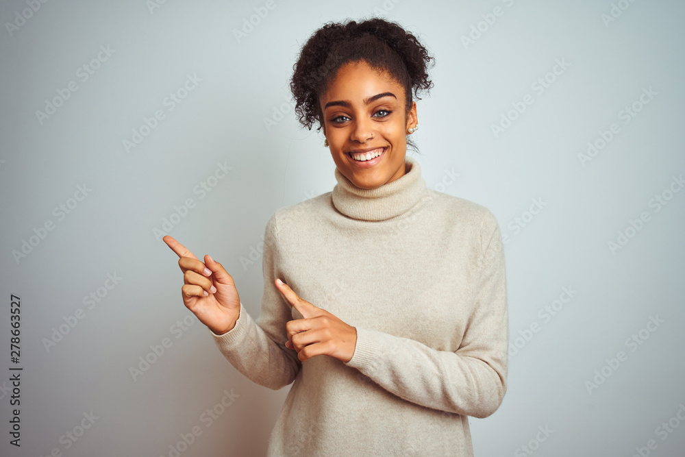 African american woman wearing winter turtleneck sweater over isolated white background smiling and looking at the camera pointing with two hands and fingers to the side. African american woman wearing winter turtleneck sweater over isolated white background smiling and looking at the camera pointing with two hands and fingers to the side.
