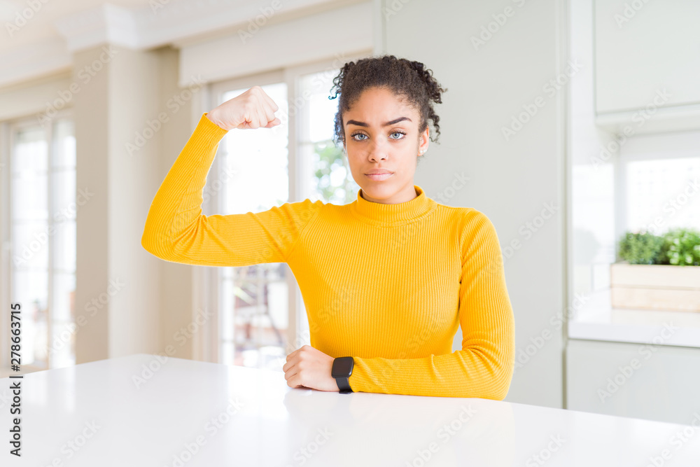 Beautiful african american woman with afro hair wearing a casual yellow sweater Strong person showing arm muscle, confident and proud of power