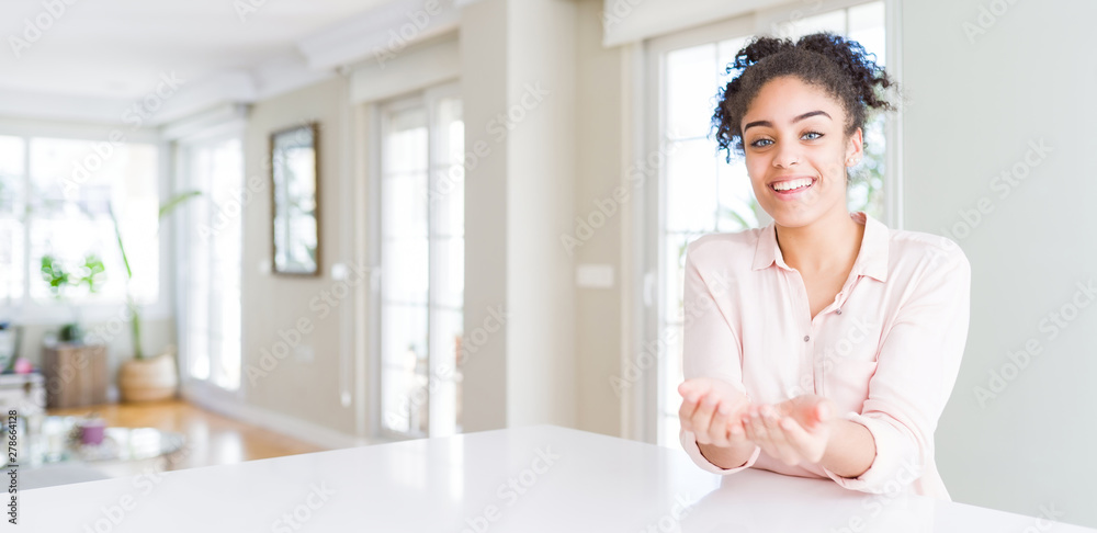 Wide angle of beautiful african american woman with afro hair Smiling with hands palms together receiving or giving gesture. Hold and protection