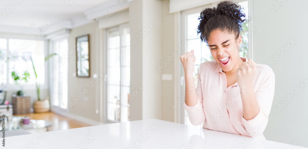 Wide angle of beautiful african american woman with afro hair very happy and excited doing winner gesture with arms raised, smiling and screaming for success. Celebration concept. Wide angle of beautiful african american woman with afro hair very happy and excited doing winner gesture with arms raised, smiling and screaming for success. Celebration concept.