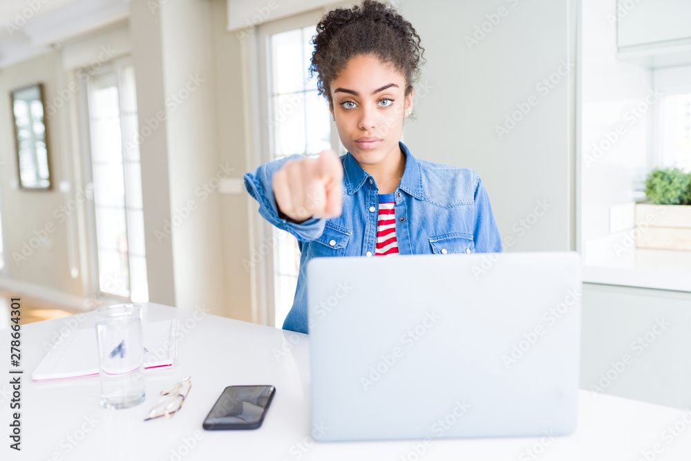 Young african american student woman using computer laptop pointing with finger to the camera and to you, hand sign, positive and confident gesture from the front Young african american student woman using computer laptop pointing with finger to the camera and to you, hand sign, positive and confident gesture from the front