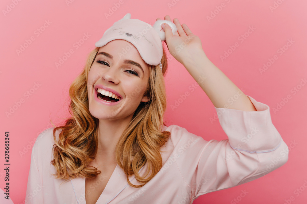Close-up shot of spectacular blonde girl laughing in good morning. Positive caucasian young lady in trendy sleepmask isolated on pink background. - obrazy, fototapety, plakaty 