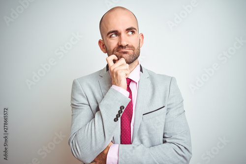 Young business man wearing suit and purple tie over isolated background with hand on chin thinking about question, pensive expression. Smiling with thoughtful face. Doubt concept.