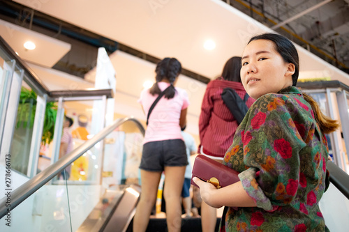 Asian woman holding her purse standing on escalator which moving up in shopping mall