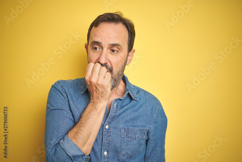 Handsome middle age senior man with grey hair over isolated yellow background looking stressed and nervous with hands on mouth biting nails. Anxiety problem.