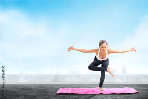 Asian healthy woman practicing yoga on the carpet at rooftop