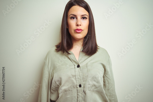 Young beautiful brunette woman wearing green shirt over isolated background with serious expression on face. Simple and natural looking at the camera.