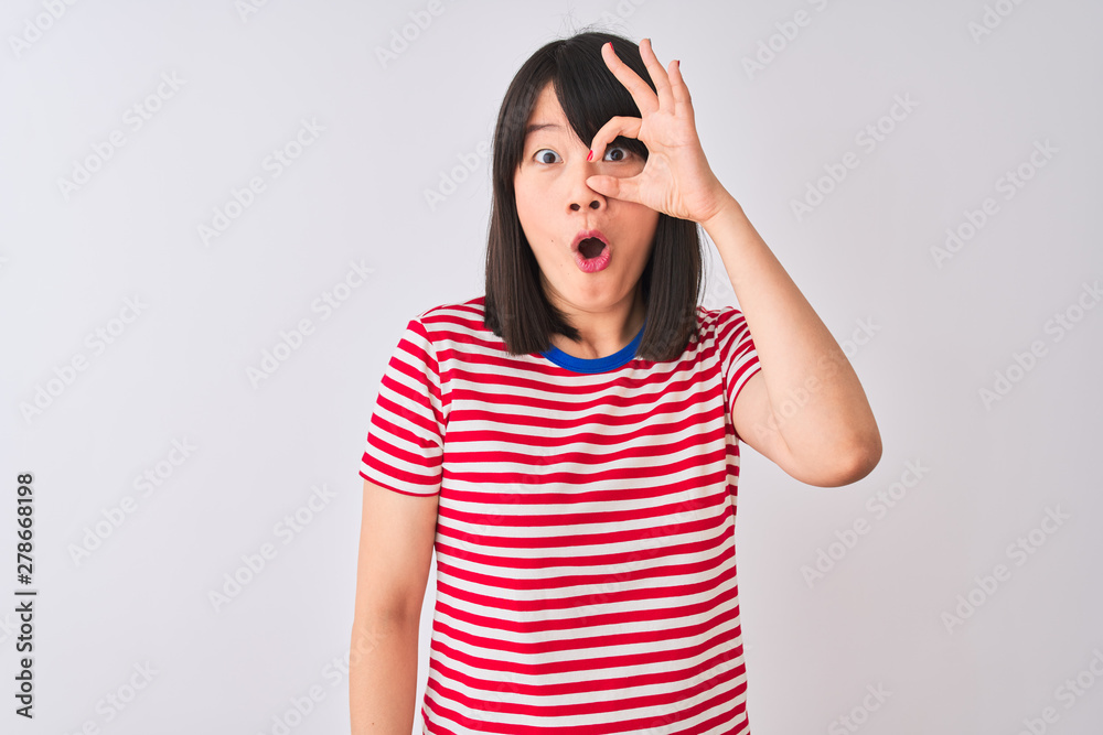Young beautiful chinese woman wearing red striped t-shirt over isolated white background doing ok gesture shocked with surprised face, eye looking through fingers. Unbelieving expression.