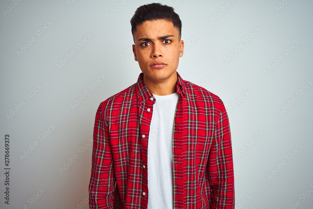 Young brazilian man wearing red shirt standing over isolated white background skeptic and nervous, disapproving expression on face with crossed arms. Negative person. Young brazilian man wearing red shirt standing over isolated white background skeptic and nervous, disapproving expression on face with crossed arms. Negative person.