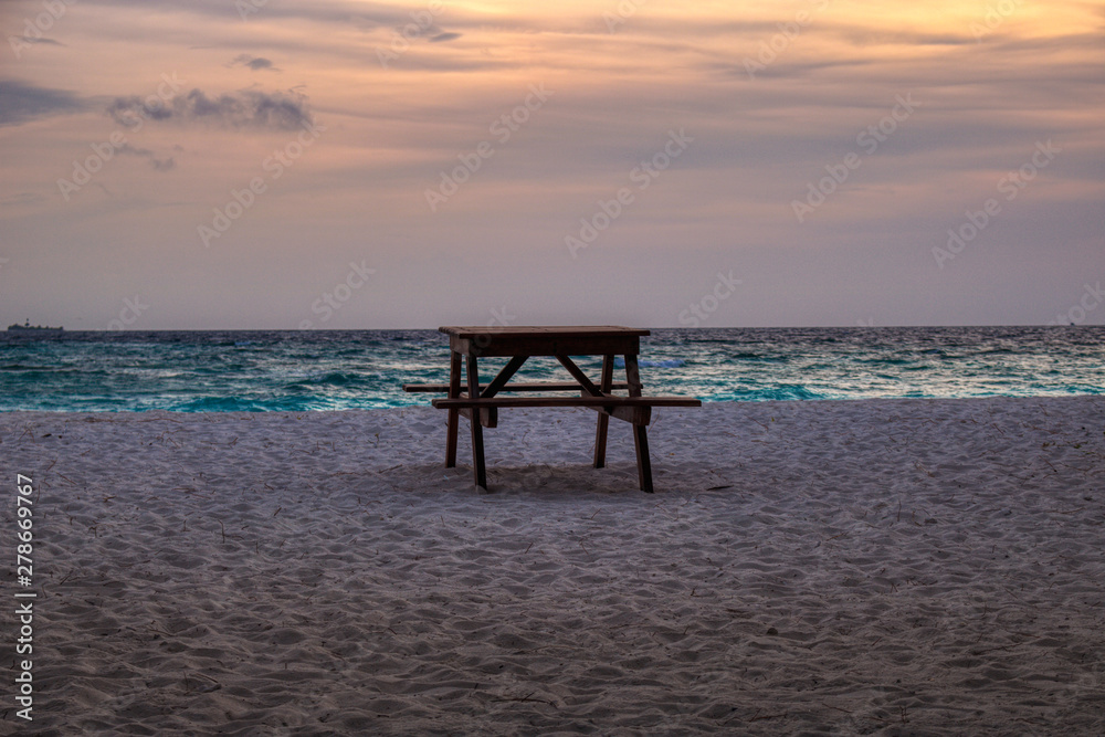 This unique photo shows a table with a bench on a beach of the Maldives during a romantic sunset
