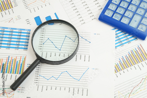 Business concept, calculator and magnifying glass on financial charts and graphs