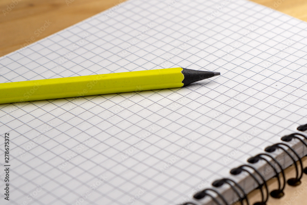 Yellow pencil on a notebook with sheets in a cage on a wooden table. Concept for shopping list, notes, planning. Side view Yellow pencil on a notebook with sheets in a cage on a wooden table. Concept for shopping list, notes, planning. Side view