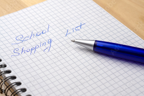 Blue pen on a notebook with sheets in a cage. Sign - school shopping list