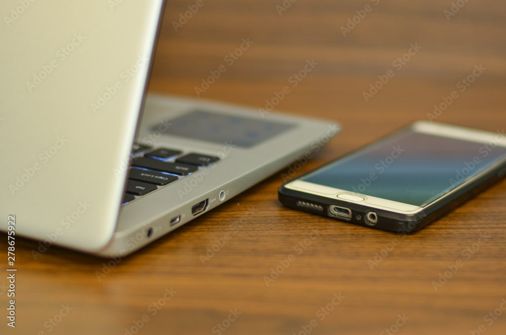 Abstract view of qwerty keyboard and a smart phone in an office setup from the back on a wooden table Abstract view of qwerty keyboard and a smart phone in an office setup from the back on a wooden table