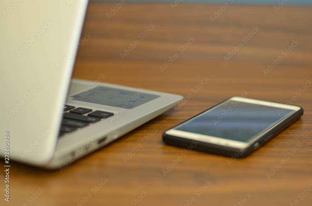 Abstract view of qwerty keyboard and a smart phone in an office setup from the back on a wooden table Abstract view of qwerty keyboard and a smart phone in an office setup from the back on a wooden table