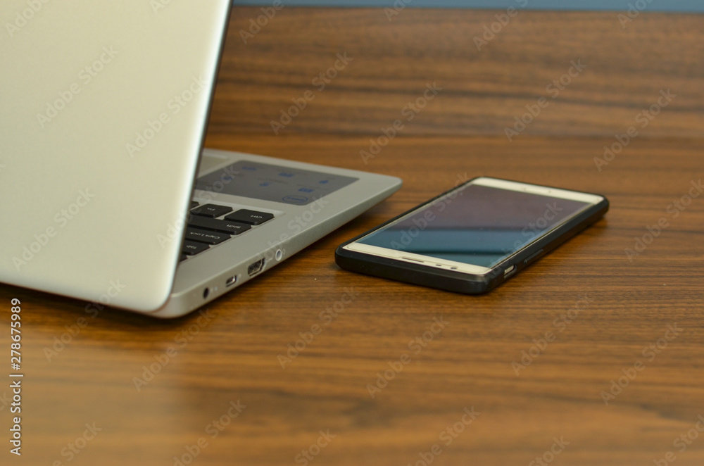 Abstract view of qwerty keyboard and a smart phone in an office setup from the back on a wooden table Abstract view of qwerty keyboard and a smart phone in an office setup from the back on a wooden table
