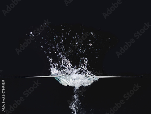 Water splash on liquid surface isolated on black background, close up view. Water bubbles in air and underwater. Abstract background for overlays design, screen blending mode layer