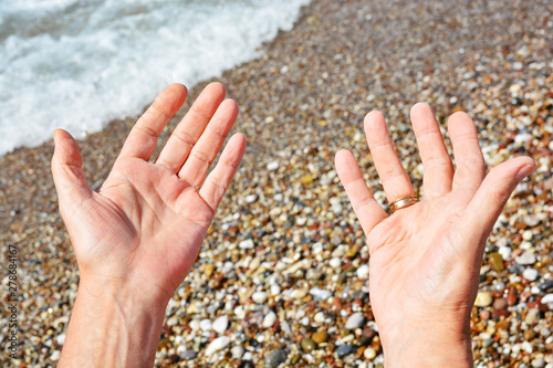 Men's tanned hands, make different compositions of fingers on the background of sea pebbles