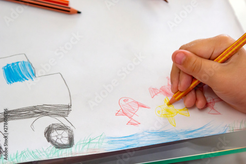 Child draws with colorful pencils. Children's drawing on theme of fishing with goldfish, car