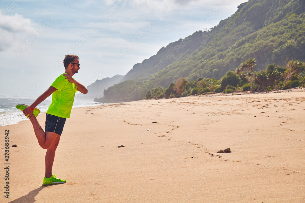 Sportsman stretching on a tropical sandy beach.