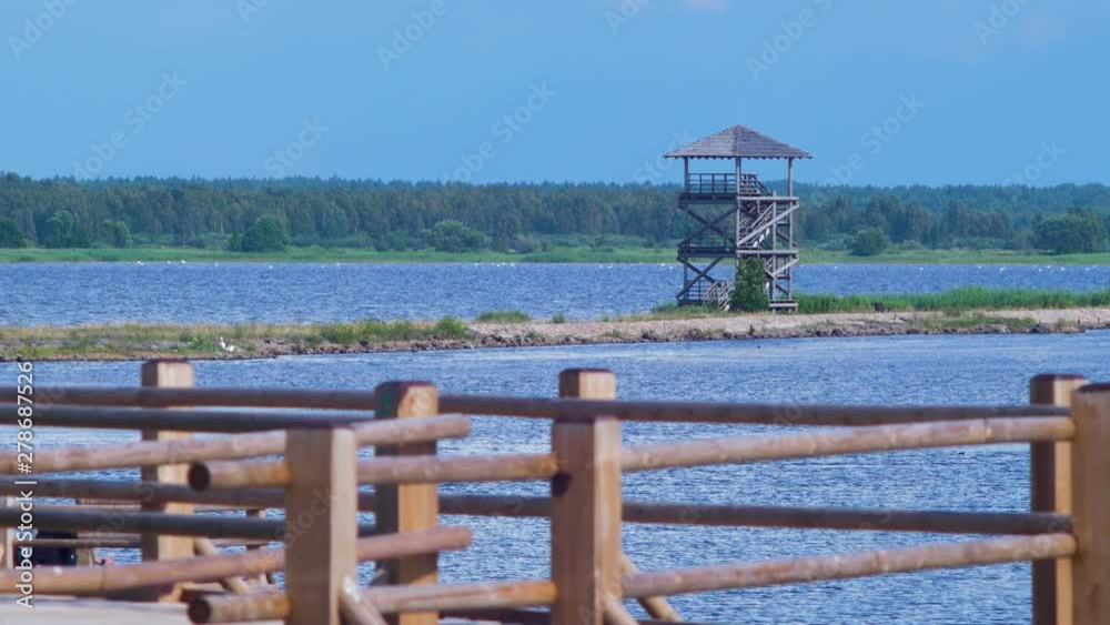 View of footbridge path and birdwatching tower at lake Liepaja in sunny summer day with scenic cumulus clouds, medium shot View of footbridge path and birdwatching tower at lake Liepaja in sunny summer day with scenic cumulus clouds, medium shot