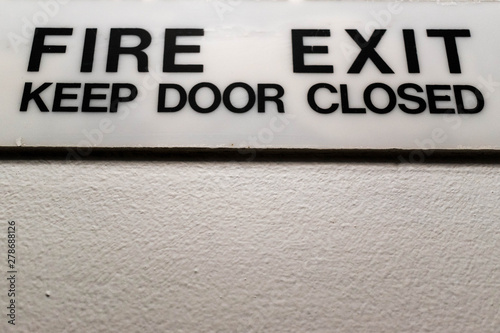 Fire exit keep door closed sign. Well lit white sign with strong black font on a white wall.