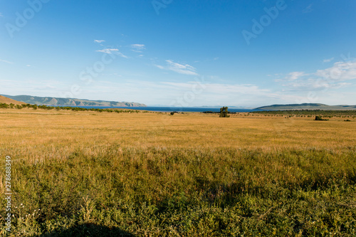 Blue sky with white clouds  trees  fields and meadows with green grass  against the mountains. Composition of nature. Rural summer landscape.