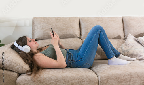 Teenage girl lying on the couch of her home looking at her phone