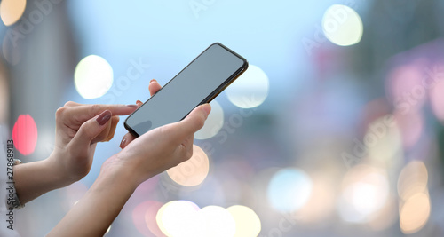 Female hands holding blank screen smartphone with blurred bokeh background..