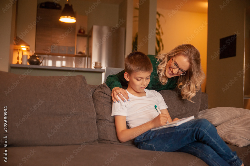 two people, young woman and boy, together happy, while doing homework in their living room.