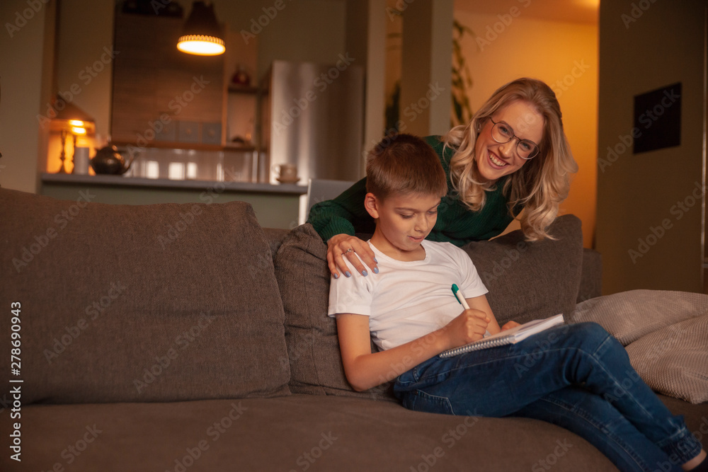 two people, young woman and boy, together happy, while doing homework in their living room, looking at camera.