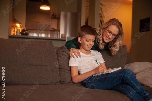 two people, young woman and boy, together happy, while doing homework in their living room.