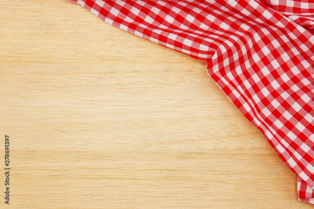 Wrinkled red gingham fabric on rustic light brown wood background, with