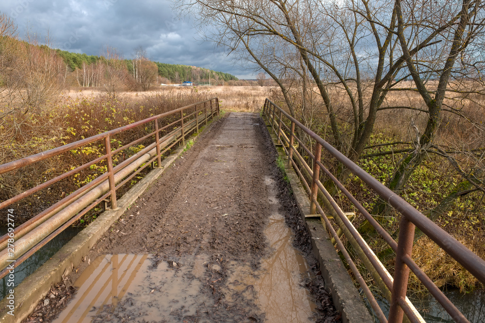 Pedestrian bridge over the river with traces of tread machines on an autumn afternoon Pedestrian bridge over the river with traces of tread machines on an autumn afternoon