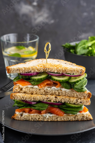 Sandwiches with cream cheese, salmon and spinach on a dark background.