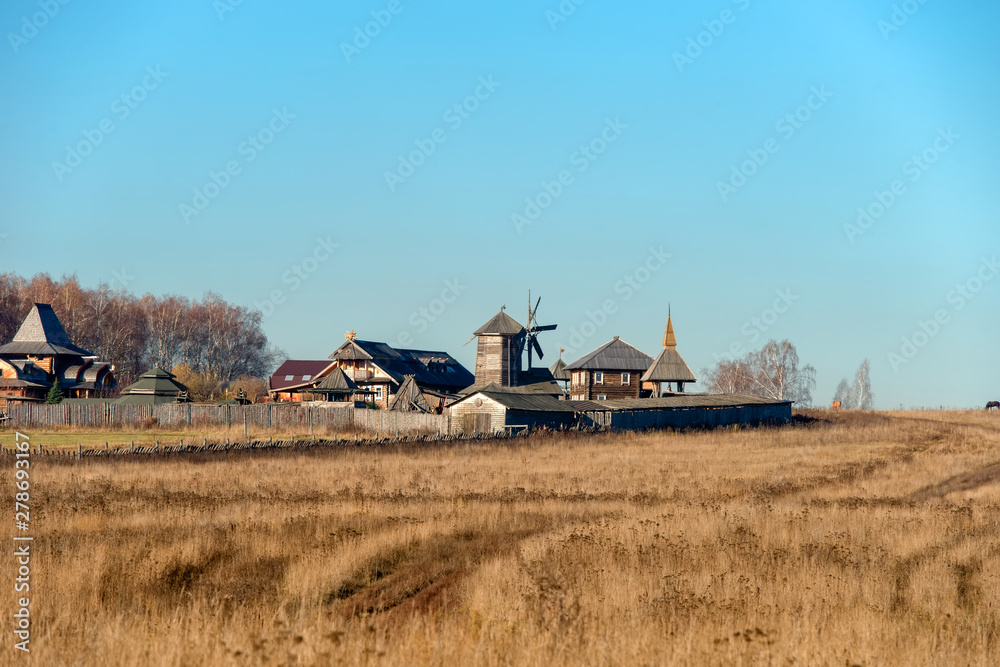 Fototapeta premium Autumn landscape. The road through the field to the entrance gate and the wooden wall of the Slavic Kremlin