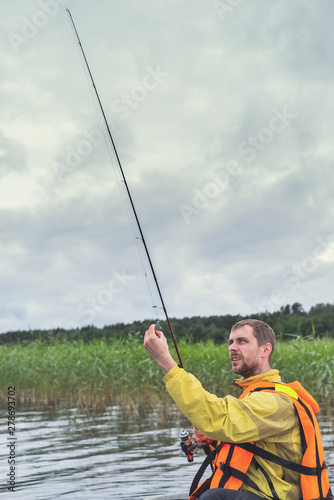 Fisherman sitting in an old wooden boat and fishing on a cloudy day.