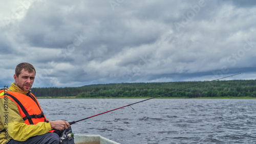 Fisherman sitting in an old wooden boat and fishing on a cloudy day.