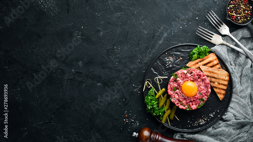 Beef steak tartare with raw egg yolk, pickled cucumber and onions. French cuisine. Top view. Free space for your text. photo
