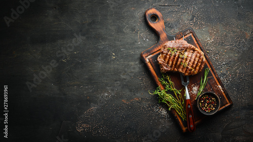 Grilled ribeye beef steak, herbs and spices on a dark table. Top view. Free space for your text.