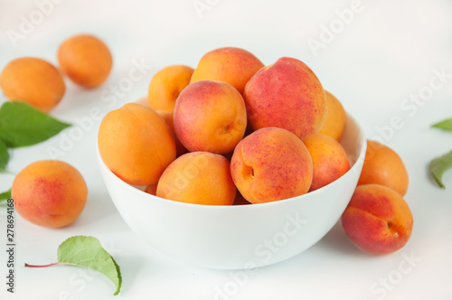 Ripe fruits of apricots with leaves in a white ceramic bowl on a white table.