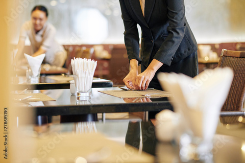 Close-up of manager laying the table at the restaurant with waitress working in the background