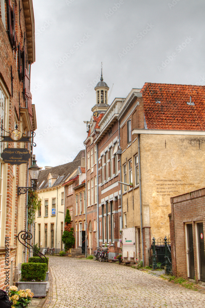 Obraz premium Idyllic street with historic houses and cobblestone pavement, in the background a churchtower; the charming Dutch city of Zutphen